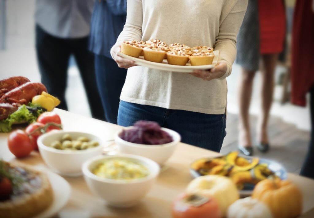 Pessoa segurando uma travessa de muffins em um evento social com diversas opções de alimentos.