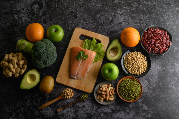 Alimentos termogênicos dispostos em uma mesa, incluindo salmão, laranja, abacate, brócolis, maçã e legumes.