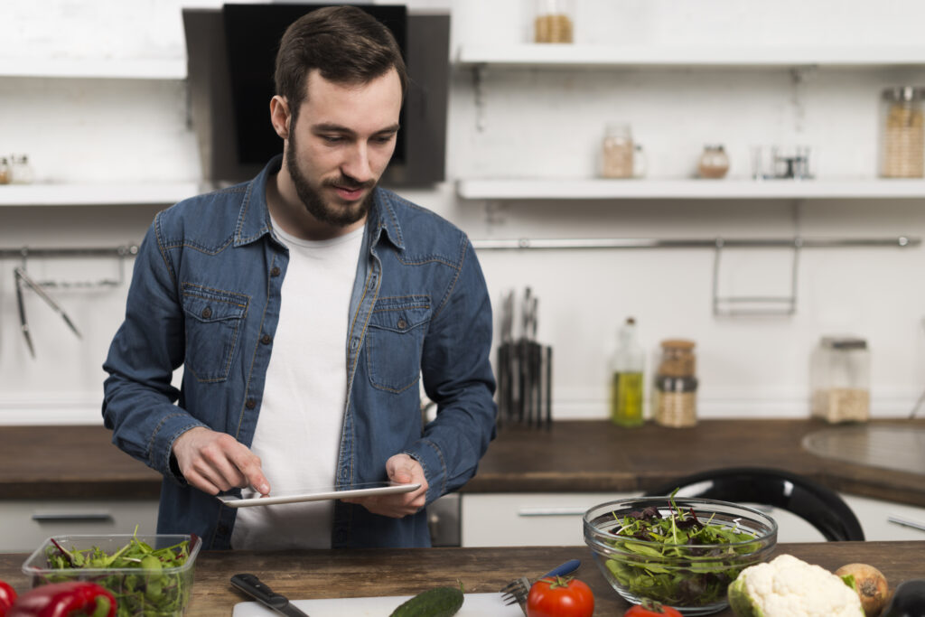 Homem planejando refeições saudáveis e econômicas na cozinha com tablet.