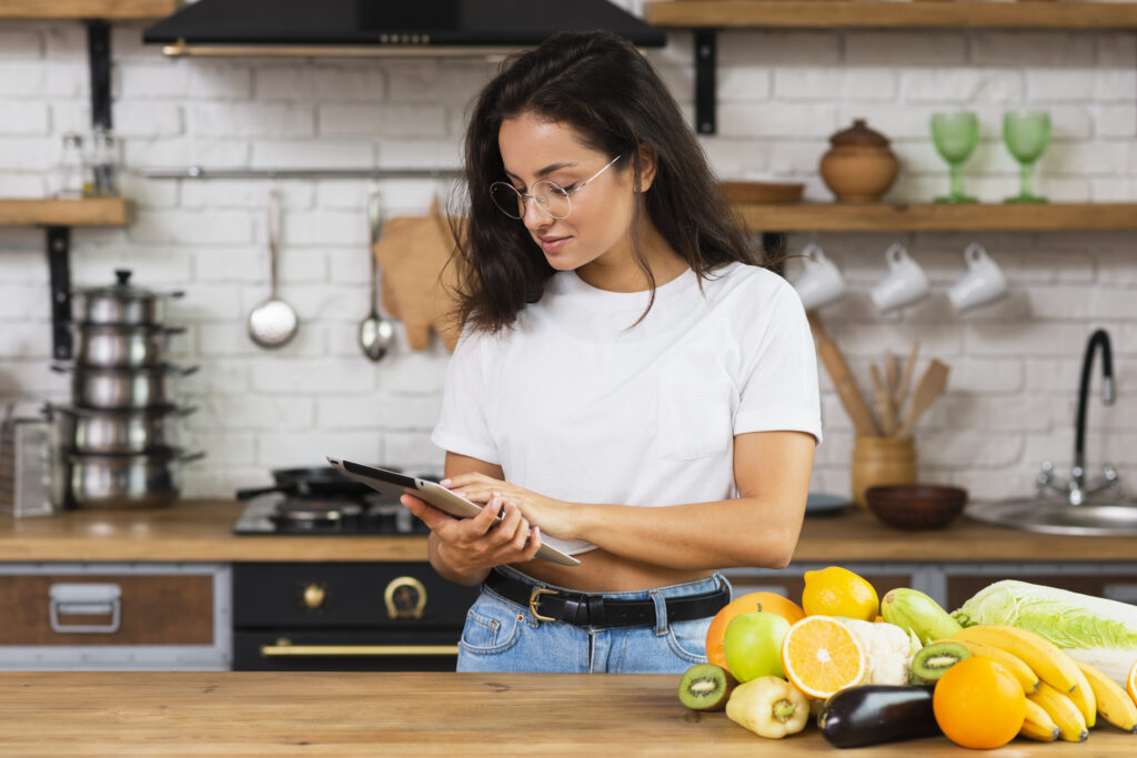 Mulher planejando refeições saudáveis com tablet na cozinha.