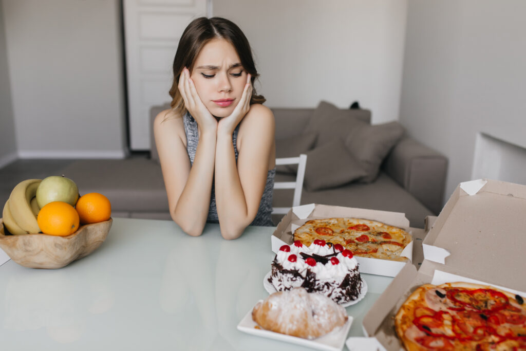 Mulher indecisa entre frutas e alimentos pouco saudáveis