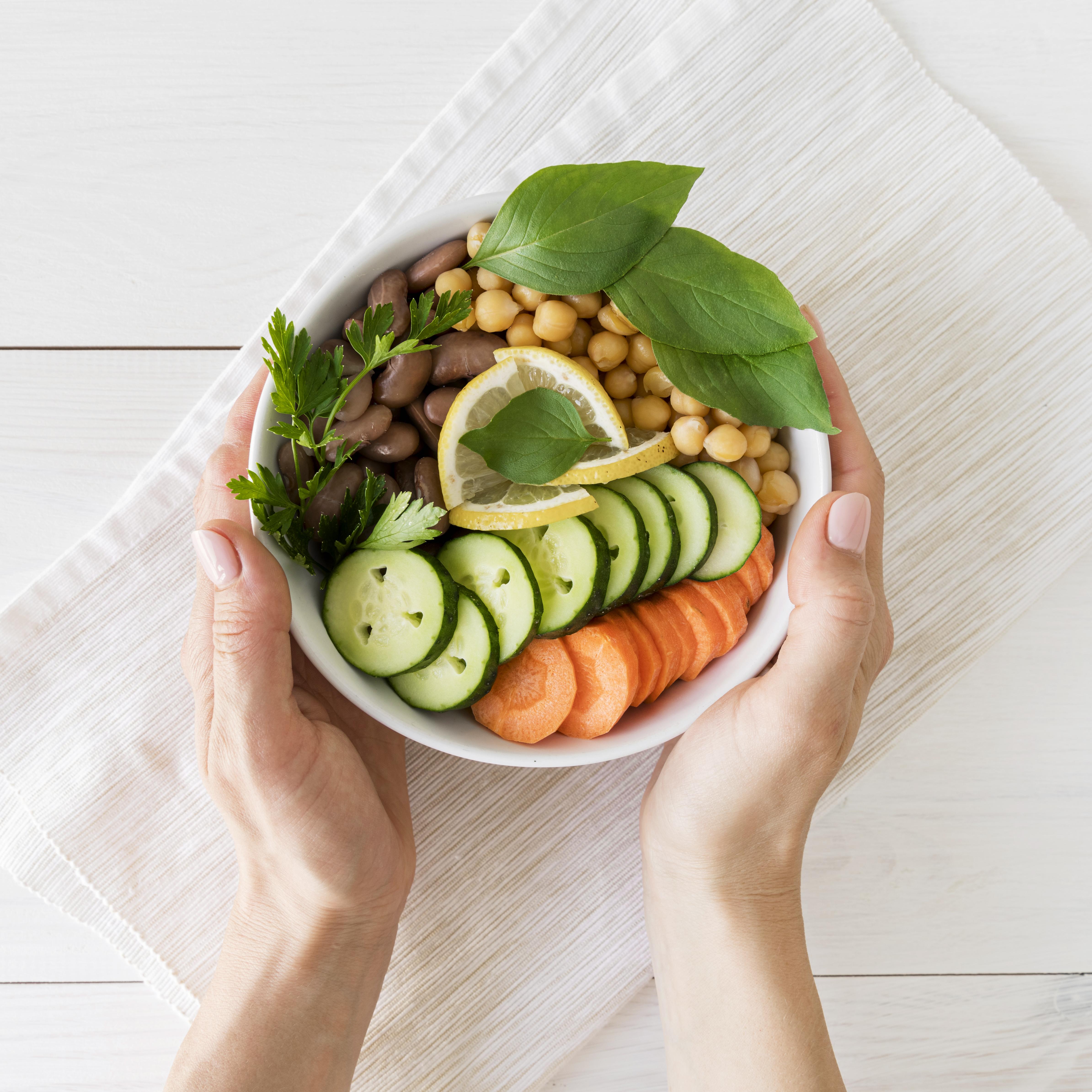 Tigela de vegetais frescos com grão-de-bico, pepino, cenoura e folhas verdes, representando uma dieta vegetariana saudável.