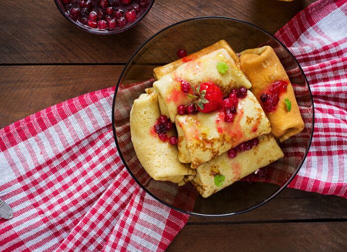 Panquecas fit recheadas com frutas vermelhas, servidas em um prato de vidro sobre uma toalha xadrez vermelha e branca.