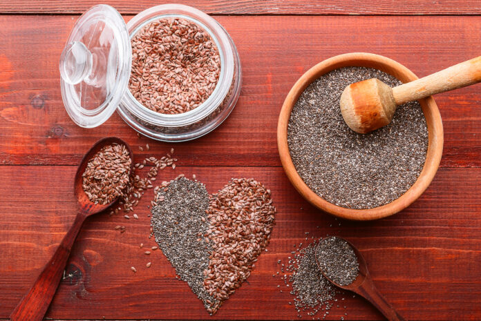 Sementes de chia e linhaça em recipientes sobre uma mesa de madeira com formato de coração.