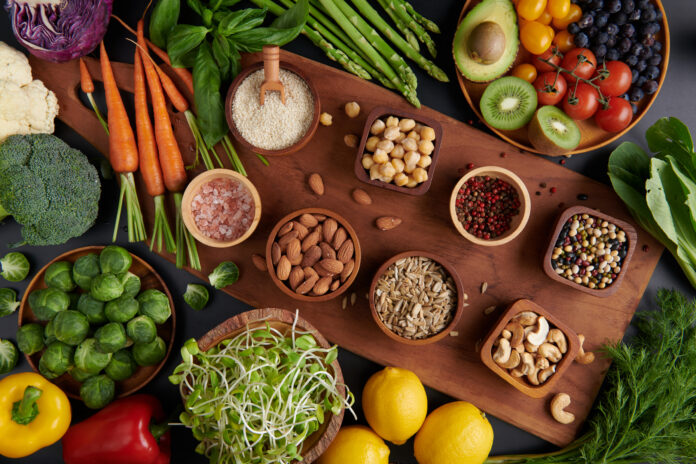 Mesa com superalimentos saudáveis, incluindo legumes, frutas, sementes e nozes dispostos em tigelas de madeira.