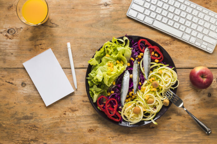 Prato de comida saudável com teclado e bloco de notas ao lado, representando alimentação e produtividade no trabalho.