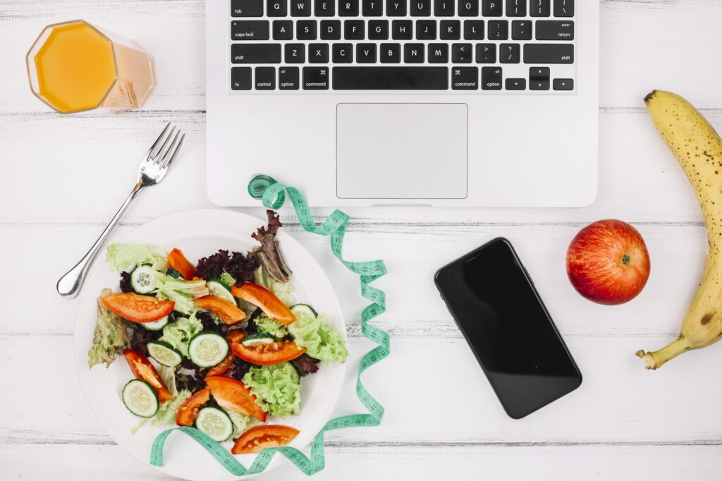 Prato de salada saudável com laptop, smartphone e frutas, representando alimentação e produtividade no trabalho.