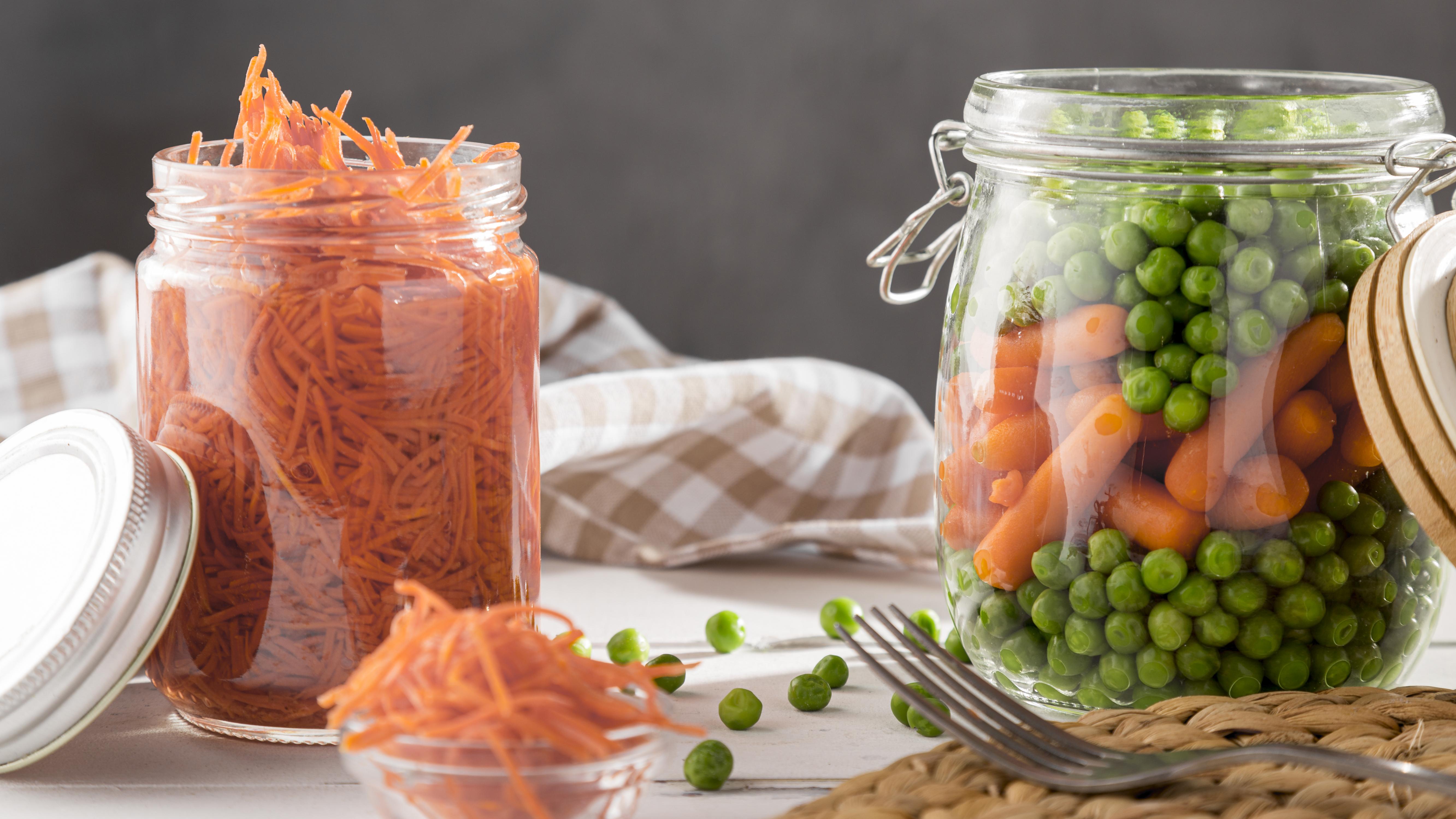 Potes de vegetais fermentados, incluindo cenouras raladas e uma mistura de ervilhas e mini cenouras.