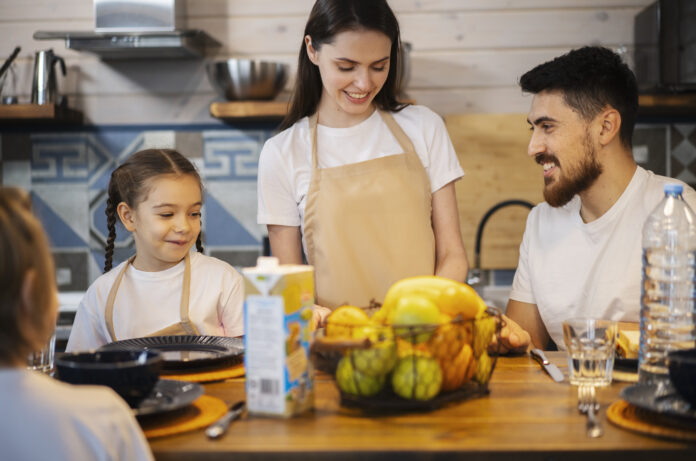 Família reunida em uma cozinha aconchegante preparando refeições saudáveis com frutas frescas sobre a mesa.