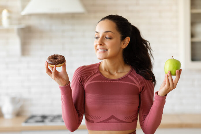 Mulher segurando um donut e uma maçã, simbolizando a escolha entre um lanche saudável e indulgente.