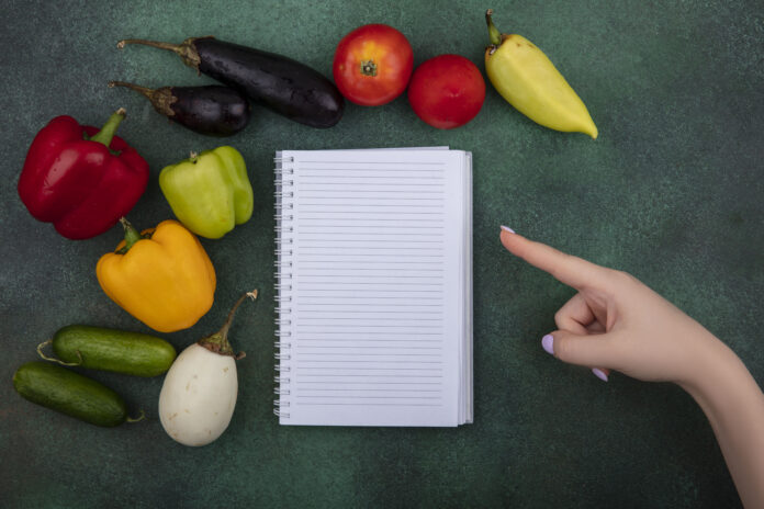 Bloco de notas vazio cercado por legumes frescos, representando planejamento de cardápio vegetariano semanal