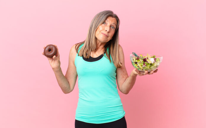 Mulher em dúvida entre uma salada e um donut, simbolizando os desafios de manter a dieta diante de gatilhos emocionais.