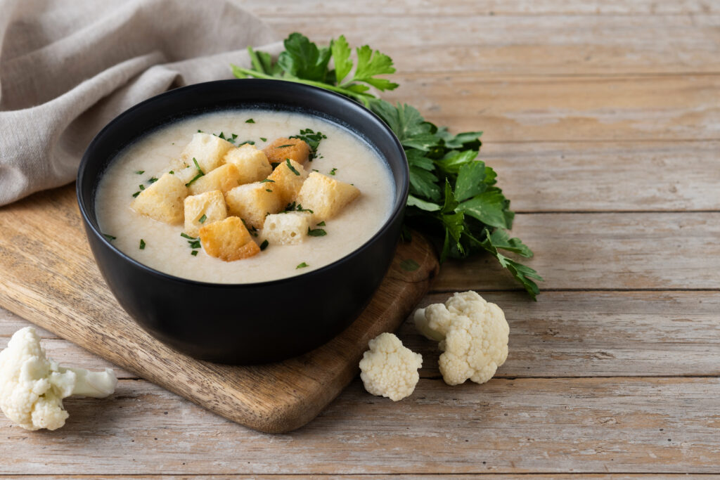 Tigela de sopa low carb com croutons e couve-flor fresca em uma mesa de madeira.