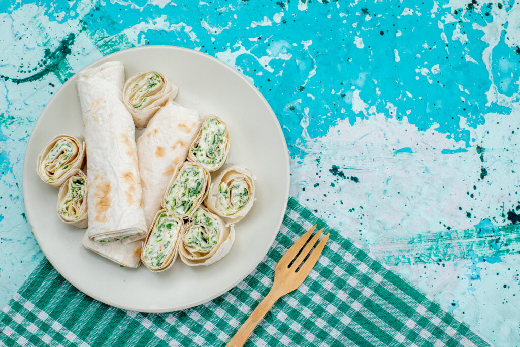 Deliciosos wraps fit de frango com molho de iogurte natural, servidos em um prato branco sobre uma toalha xadrez verde.