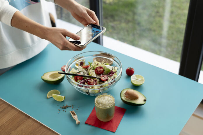 Pessoa fotografando uma salada fresca com abacate, tomate e limão sobre uma mesa azul, representando uma refeição saudável da Dieta DASH.