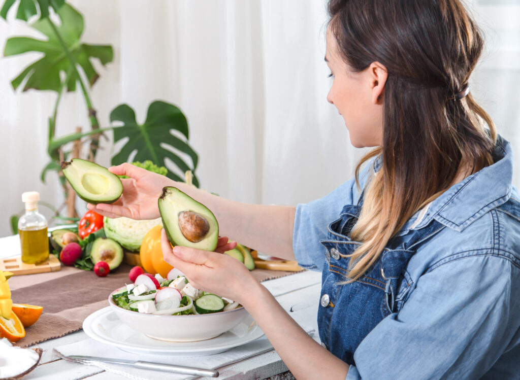 Mulher preparando uma salada saudável com abacate e vegetais frescos.