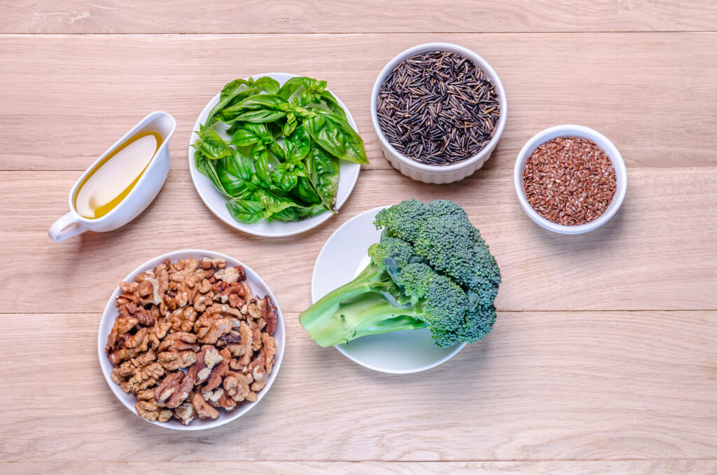 Ingredientes saudáveis como nozes, brócolis, sementes de linhaça, manjericão fresco e azeite, representando opções para uma dieta baseada em plantas.