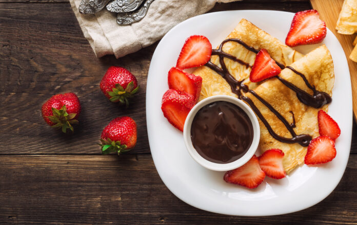 Panqueca doce fit de cacau com morangos e calda de chocolate em prato decorado.