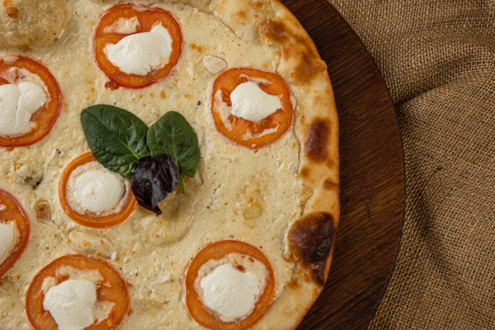 Pizza de tapioca com queijo branco e rodelas de tomate, decorada com folhas frescas.