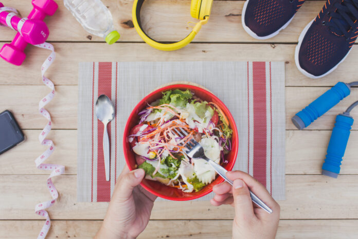 Salada colorida como refeição saudável para dias de treino intenso, cercada por itens de fitness.