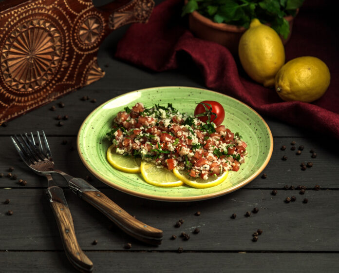 Salada de grão-de-bico com atum e molho de limão, decorada com fatias de limão e servida em um prato verde.