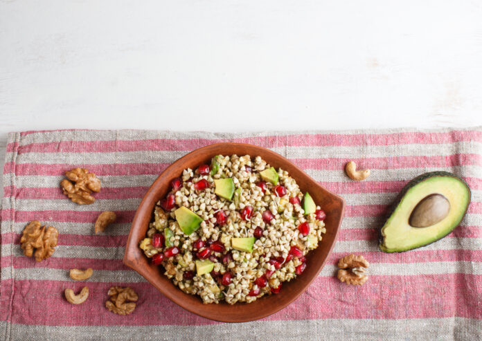 Tigela de salada de grãos integrais com abacate, romã e nozes em um fundo de tecido listrado.