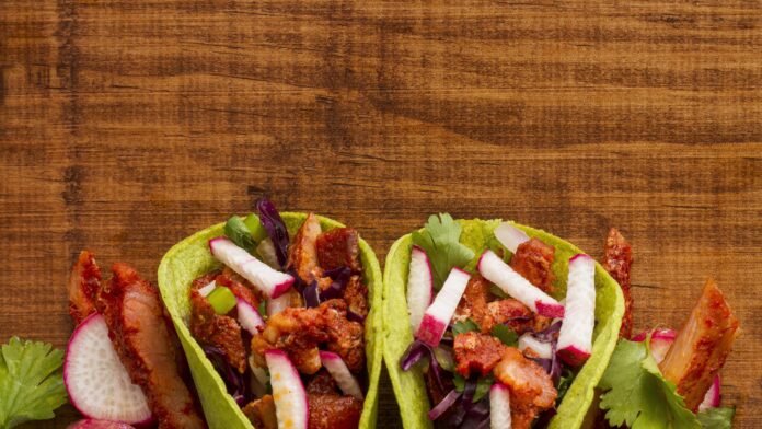 Tacos fit de frango com abacate e vegetais frescos em uma mesa de madeira.