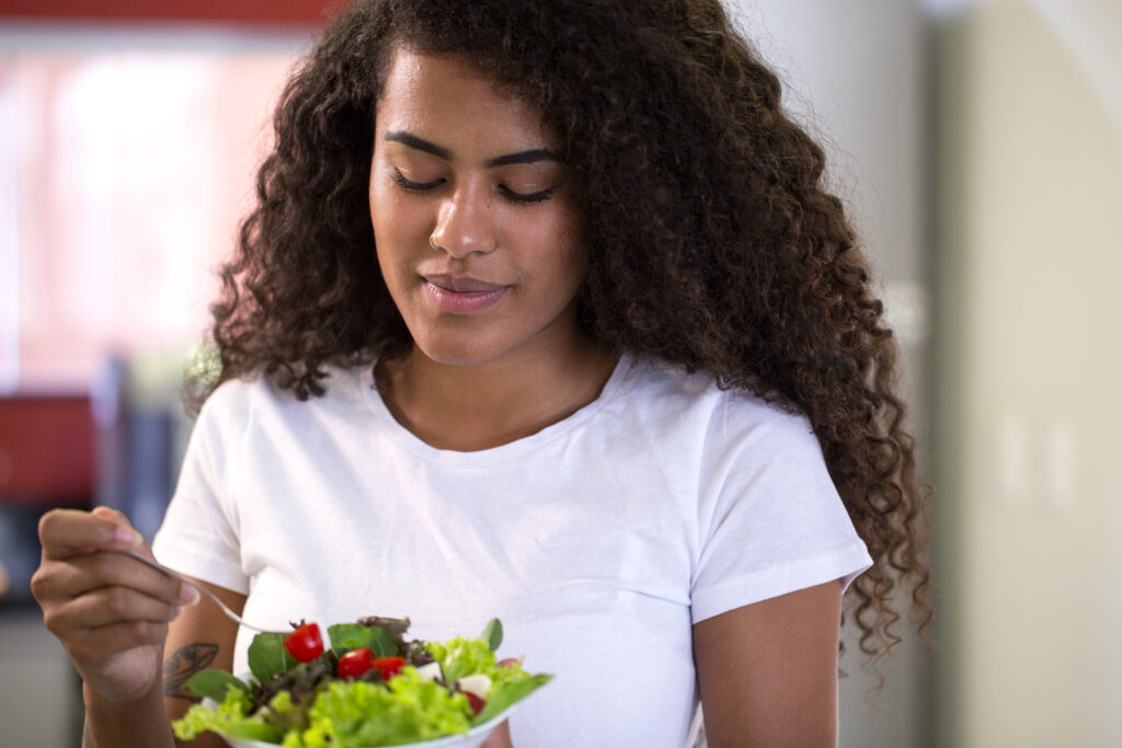 Mulher com cabelos cacheados segurando uma salada fresca, destacando a prática da alimentação intuitiva.