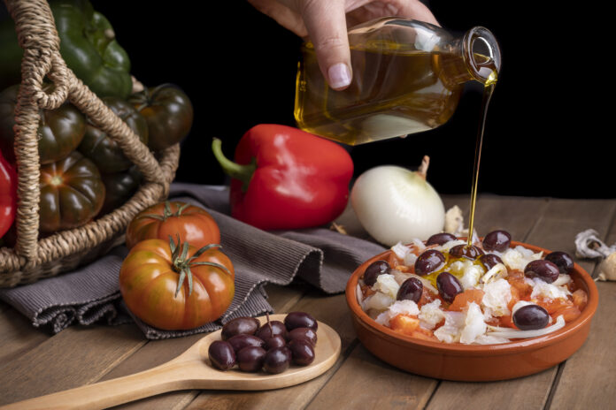 Cesta de vegetais frescos com azeite de oliva sendo derramado sobre um prato mediterrâneo.