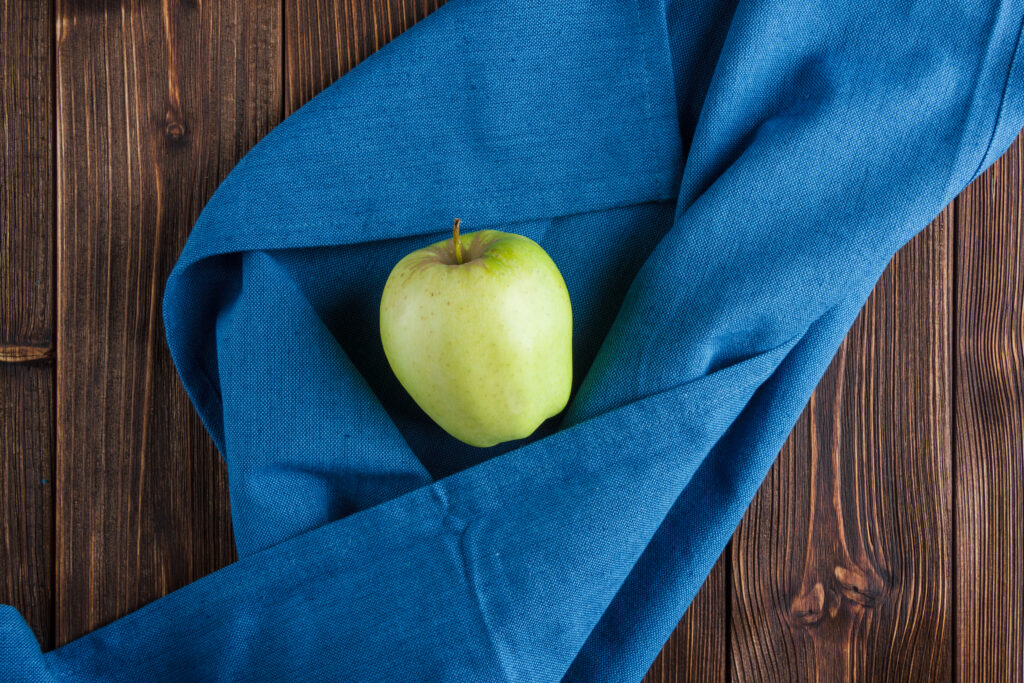 Maçã verde sobre tecido azul, representando simplicidade e saúde na dieta das zonas azuis.