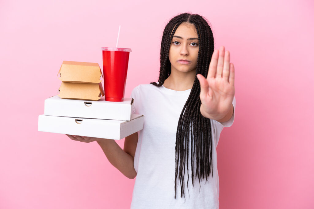 Mulher com caixas de fast food e copo de bebida faz sinal de "pare", simbolizando controle alimentar em festas e ocasiões especiais.