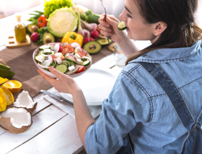 Mulher apreciando uma salada saudável com alimentos frescos ao fundo, simbolizando a prática da alimentação intuitiva.