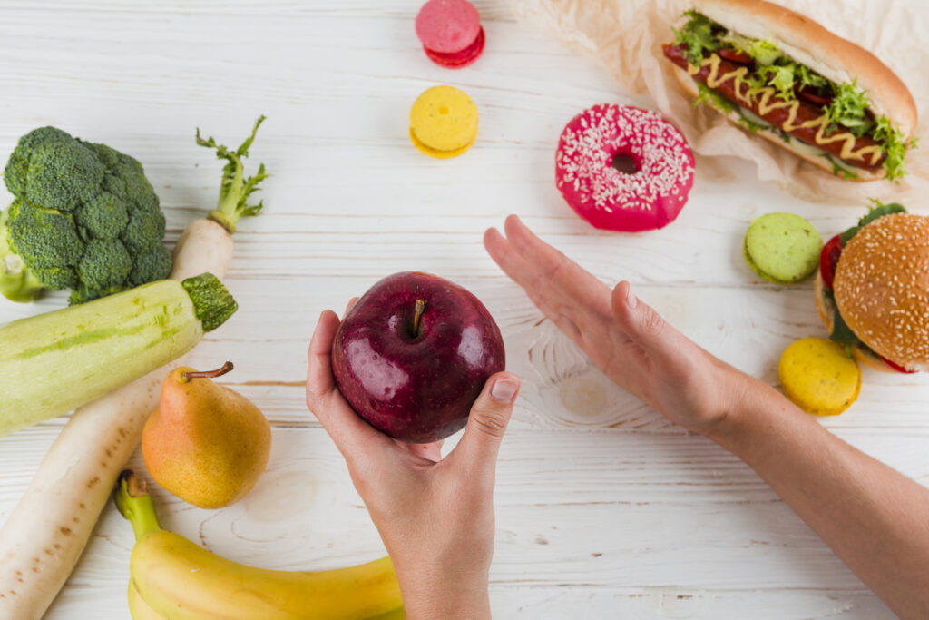 Uma pessoa segurando uma maçã enquanto recusa alimentos processados, representando escolhas alimentares saudáveis.